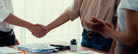 Analyst team celebrates successful data analysis with handshake. Panorama shot handshaking after adjusting attitude or brainstorm for future success in meeting room with BI dashboard paper. Scrutinizeの写真素材