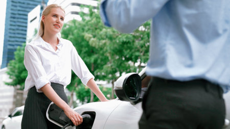 Progressive businessman and businesswoman install charger plug from charging station to electric car before driving around city center. Eco friendly rechargeable car powered by clean energy.の写真素材