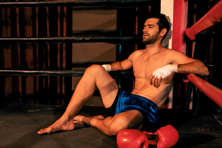 Tired and exhausted caucasian boxer removed his boxing glove and sitting, resting on the edge of the ring after intense training or fighting match. Impetusの写真素材
