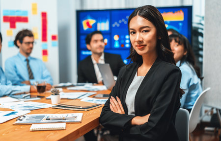 Portrait of happy young asian businesswoman or analyst looking at camera with her colleague analyzing data analysis in dynamic business strategy investment planning meeting. Habilimentの写真素材
