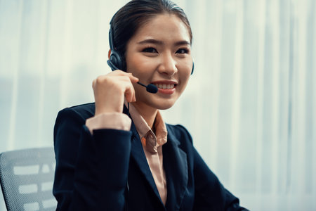 Asian call center with headset and microphone working on her workspace looking at camera. Female operator provide exceptional customer service. Supportive call center agent portrait. Enthusiasticの写真素材