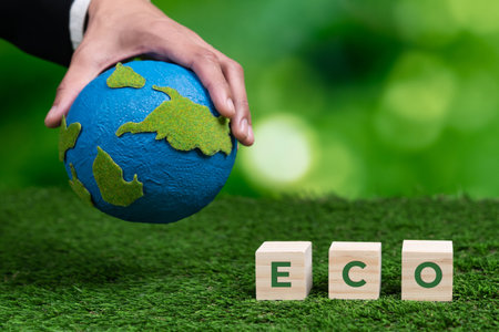 Businessman hand holding wooden cube with eco symbol and paper globe on fertile soil background. Environmental awareness and sustainable energy. Clean and renewable energy for greener ecology. Alterの写真素材