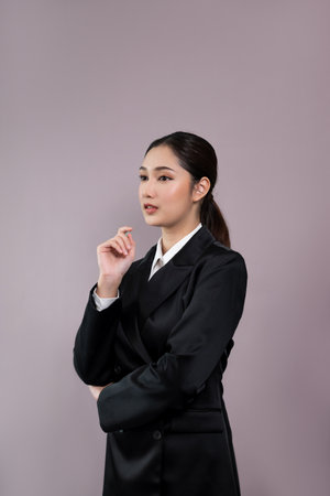 Confident young businesswoman stands on isolated background, posing in formal black suit. Office lady or manager with smart and professional appearance. Enthusiasticの写真素材