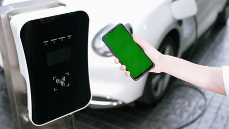 Mockup phone with green screen display energy status of electric vehicle connected to charging station for copyspace. Progressive concept for clean environment. EV powered by green renewable energy.の写真素材