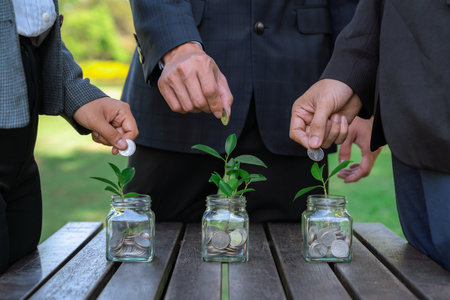 Business people put coin to money saving glass jar on outdoor table as sustainable money growth investment or eco-subsidize. Green corporate promot and invest in environmental awareness. Gyreの写真素材
