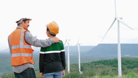 Engineer with his son on a wind farm atop a hill or mountain in the rural. Progressive ideal for the future production of renewable, sustainable energy. Energy generation from wind turbine.の写真素材