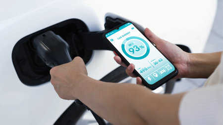 Hand insert EV charger to electric car to recharge battery while check battery status display on...