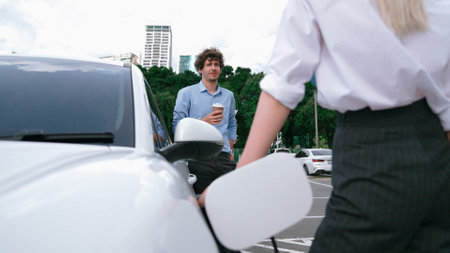 Progressive businessman and businesswoman leaning on electric car connected to charging station before driving around city center. Eco friendly rechargeable car powered by clean energy.の写真素材