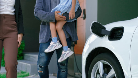 Progressive young parents and daughter living in a home with an electric vehicle and electronic vehicle charging station. Green and clean energy from electric vehicles for healthy environment.の写真素材
