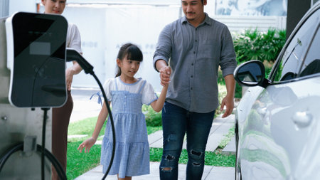 Progressive parent have returned from picking up daughter at school with concept of electric vehicle and renewable energy, charging station for EV car at home. Alternative eco transportation.の写真素材