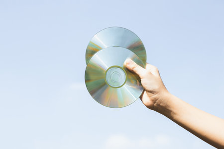 Recyclable CD disk or electric waste held in hand up on sky background. Hand holding electronic trash for recycle reduce and reuse concept to promote clean environment with recycling management. Gyreの写真素材