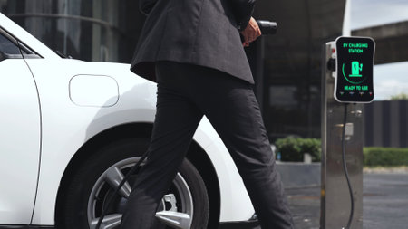 Businessman recharge his electric car from charging station at city center or public car park. Eco...