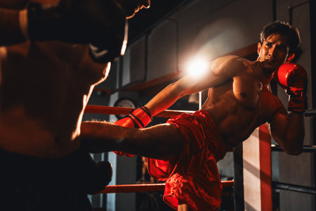 Asian and Caucasian Muay Thai boxer unleash kick attack in fierce boxing match. Thai boxer with strong muscular body exchanging punch and kick strike with relentless combat prowess. Impetusの写真素材