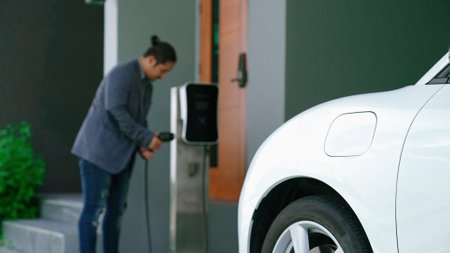 Progressive man attaches an emission-free power connector to the battery of electric vehicle at his home. Electric vehicle charging via cable from charging station to EV car batteryの写真素材