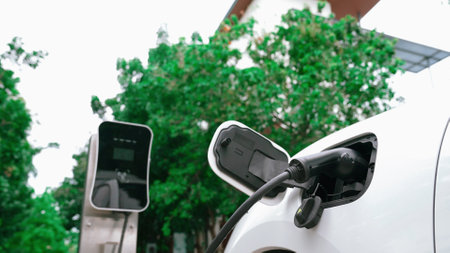 Progressive sustainability of energy concept by electric car parking and recharging next to home charging station. Electric vehicle driven by renewable energy for environmental preservation.の写真素材
