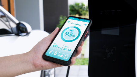 Smartphone display battery status on smart EV mobile application while EV car recharging electricity by home charging station in garage. Future innovative EV car and energy sustainability. Peruseの写真素材
