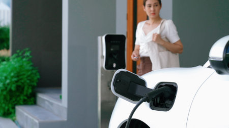Progressive lifestyle of a modern woman who have just returned from work in an electric vehicle that is being charged at home. Electric vehicle powered by sustainable clean energy.の写真素材