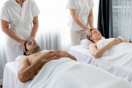 Caucasian couple enjoying relaxing anti-stress head massage and pampering facial beauty skin recreation leisure in dayspa modern light ambient at luxury resort or hotel spa salon. Quiescentの写真素材