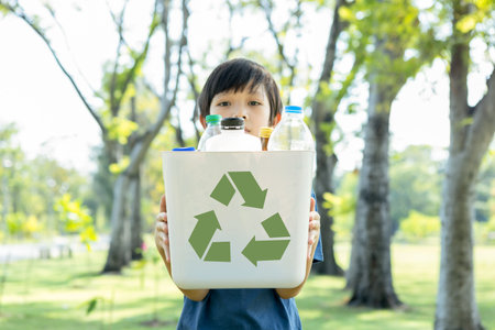 Cheerful young asian boy holding recycle symbol bin on daylight natural green park promoting waste recycle, reduce, and reuse encouragement for eco sustainable awareness for future generation. Gyreの写真素材