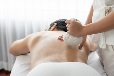 Hot herbal ball spa massage body treatment, masseur gently compresses herb bag on man body. Tranquil and serenity of aromatherapy recreation in day lighting ambient at spa salon. Quiescentの写真素材