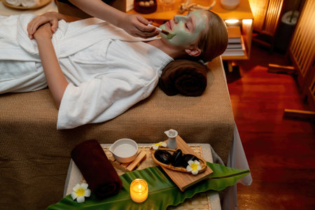 Serene ambiance of spa salon, woman customer indulges in rejuvenating with luxurious face cream massage with warm lighting candle. Facial skin treatment and beauty care concept. Quiescentの写真素材