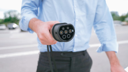 Progressive businessman install charger plug from charging station to his electric car before driving around city center. Eco friendly rechargeable car powered by sustainable and clean energy.の写真素材