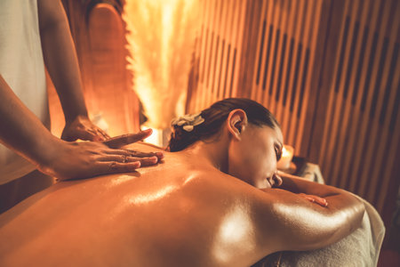 Closeup woman customer enjoying relaxing anti-stress spa massage and pampering with beauty skin recreation leisure in warm candle lighting ambient salon spa at luxury resort or hotel. Quiescentの写真素材