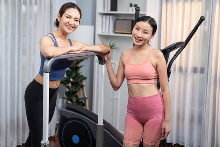 Energetic and strong athletic asian woman running on elliptical running machine at home with workout...