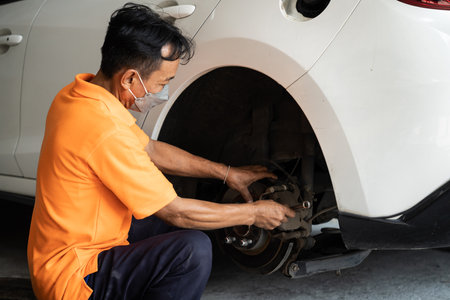 Hardworking mechanic changing car wheel in auto repair workshop. Automotive service worker changing leaking rubber tire in concept of professional car care and maintenance. Oxusの写真素材