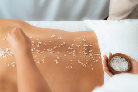 Blissful man customer having exfoliation treatment in luxury spa salon with warmth candle light ambient. Salt scrub beauty treatment in health spa body scrub. Quiescentの写真素材