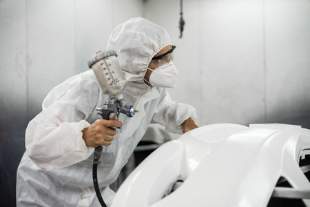 Automotive service worker in full protective gear expertly apply color paint in to cars bodywork with spray gun or respirator painting in chamber workshop. Car paint service for scratch refinish.Oxusの写真素材