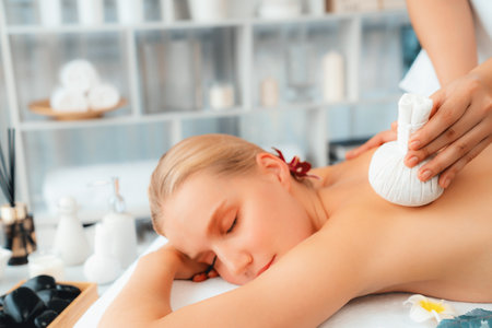Hot herbal ball spa massage body treatment, masseur gently compresses herb bag on woman body. Tranquil and serenity of aromatherapy recreation in day lighting ambient at spa salon. Quiescentの写真素材