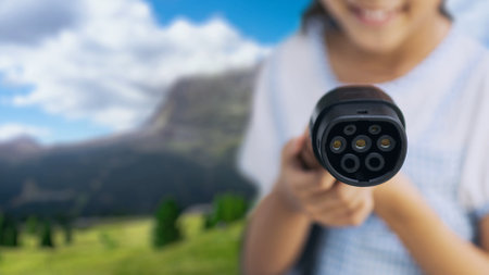 Focus EV charger pointing in front of camera with young girl in blurry nature and mountain...