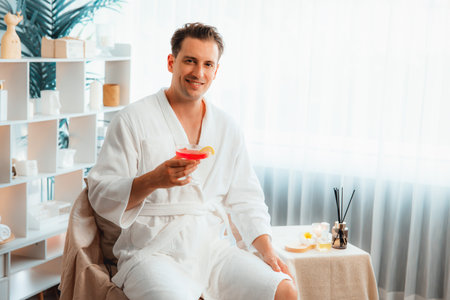 Beauty or body treatment spa salon vacation lifestyle concept with man wearing bathrobe relaxing with drinks in luxurious hotel spa or resort room. Vacation and leisure relaxation. Quiescentの写真素材