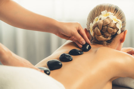 Hot stone massage at spa salon in luxury resort with day light serenity ambient, blissful woman customer enjoying spa basalt stone massage glide over body with soothing warmth. Quiescentの写真素材