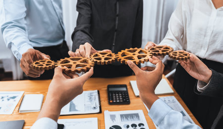 Office worker holding cog wheel as unity and system teamwork in corporate workplace with piles of business paper and financial report on meeting table. Business people with business success. Concordの写真素材