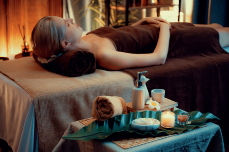 Aromatherapy massage ambiance or spa salon composition setup with focus decor candles and spa accessories on blurred woman enjoying blissful aroma spa massage in resort or hotel background. Quiescentの写真素材