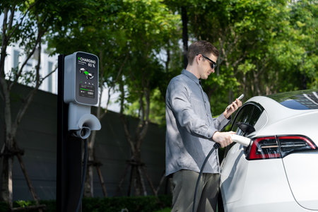 Young man travel with EV electric car charging in green sustainable city outdoor garden in summer shows urban sustainability lifestyle by green clean rechargeable energy of electric vehicle innardsの写真素材