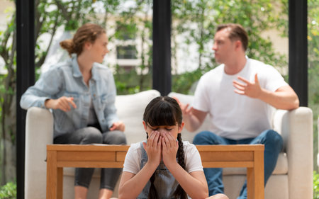 Stressed and unhappy young girl crying and trapped in middle of tension by her parent argument in living room. Unhealthy domestic lifestyle and traumatic childhood develop to depression. Synchronosの写真素材