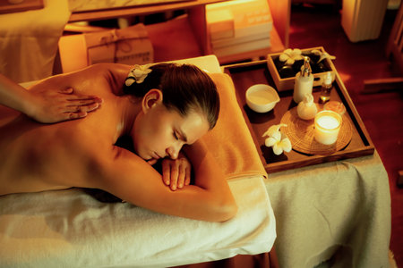 Caucasian woman customer enjoying relaxing anti-stress spa massage and pampering with beauty skin recreation leisure in warm candle lighting ambient salon spa at luxury resort or hotel. Quiescentの写真素材