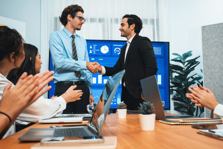 Two businessman shake hand in meeting room with coworker give cheerful applause. Team of analyst celebrate after successful significant progress on business strategic performance. Habilimentの写真素材