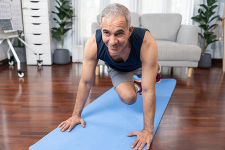 Athletic and active senior man doing exercise on fit mat with plank climbing at home exercise as concept of healthy fit body lifestyle after retirement. Cloutの写真素材