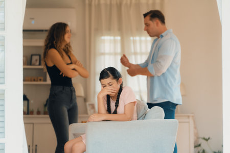 Annoyed and unhappy young girl sitting on sofa trapped in middle of tension by her parent argument in living room. Unhealthy domestic lifestyle and traumatic childhood develop to depression.Synchronosの写真素材