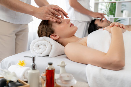 Caucasian couple enjoying relaxing anti-stress head massage and pampering facial beauty skin recreation leisure in dayspa modern light ambient at luxury resort or hotel spa salon. Quiescentの写真素材