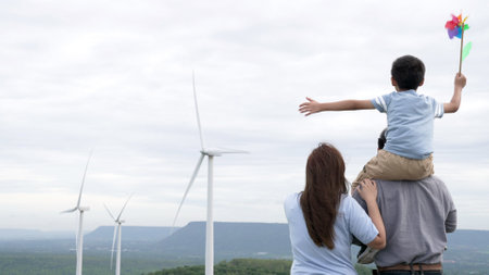 Concept of progressive happy family enjoying their time at the wind turbine farm. Electric generator from wind by wind turbine generator on the country side with hill and mountain on the horizon.の写真素材