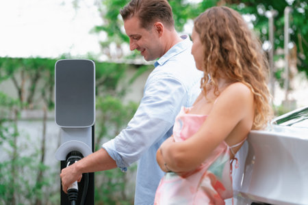 Happy and lovely couple with eco-friendly conscious recharging electric vehicle from EV charging...