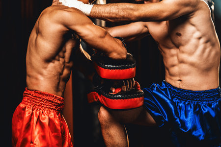 Asian and Caucasian Muay Thai boxer unleash knee attack in fierce boxing training session, delivering knee strike to sparring trainer, showcasing Muay Thai boxing technique and skill. Impetusの写真素材
