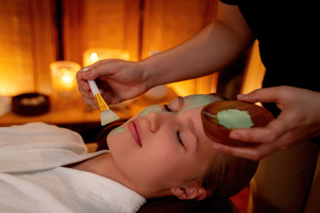 Serene ambiance of spa salon, woman customer indulges in rejuvenating with luxurious face cream massage with warm lighting candle. Facial skin treatment and beauty care concept. Quiescentの写真素材