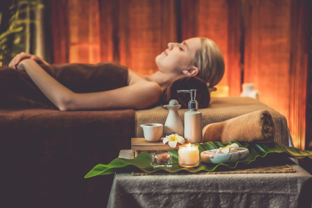 Aromatherapy massage ambiance or spa salon composition setup with focus decor candles and spa accessories on blurred woman enjoying blissful aroma spa massage in resort or hotel background. Quiescentの写真素材