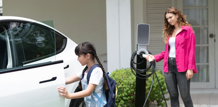 Happy little young girl learn about eco-friendly and energy sustainability as she help her mother recharge electric vehicle from home EV charging station. EV car and modern family. Panorama Synchronosの写真素材